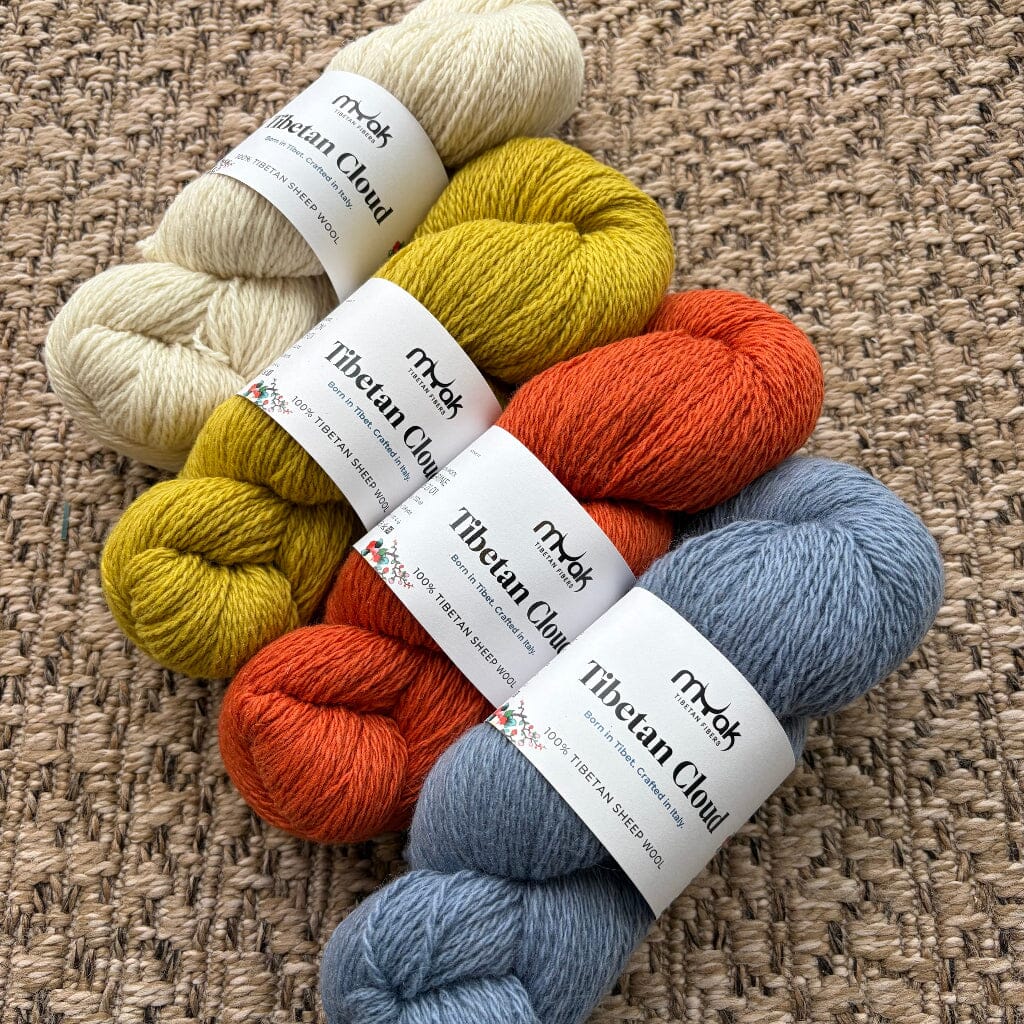 Five skeins of yarn in beige, yellow, orange, and blue on a textured surface.