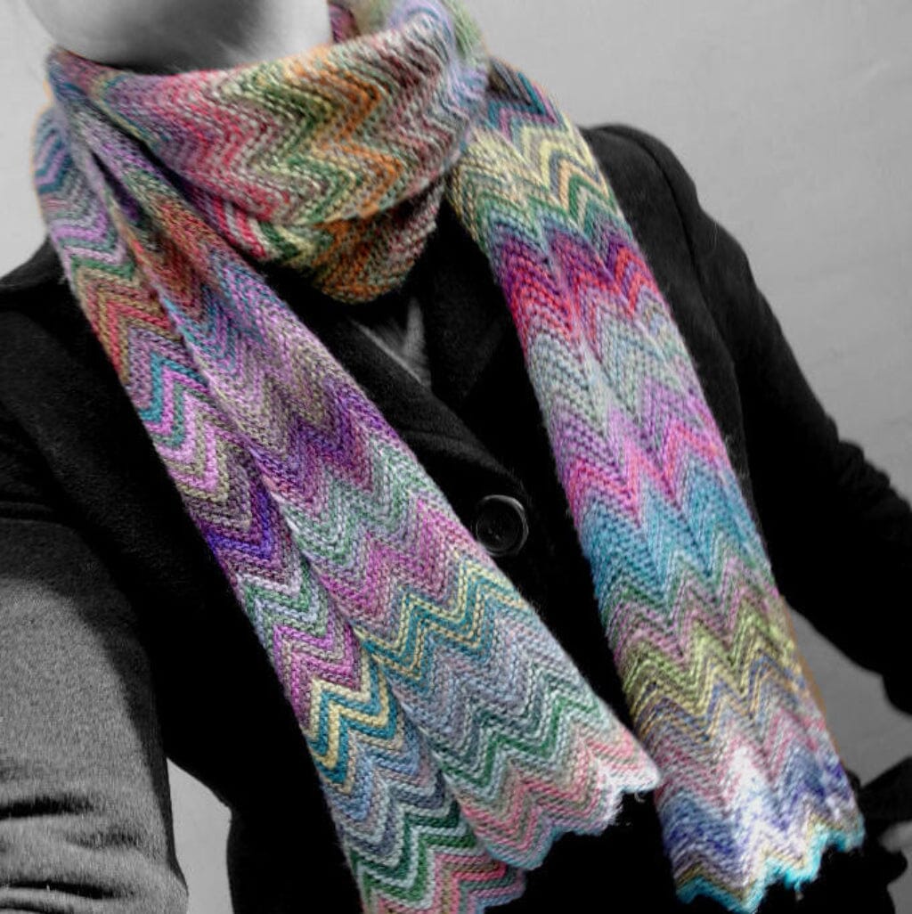 Multicolored knitted scarf with a zigzag pattern worn by a person against a neutral background