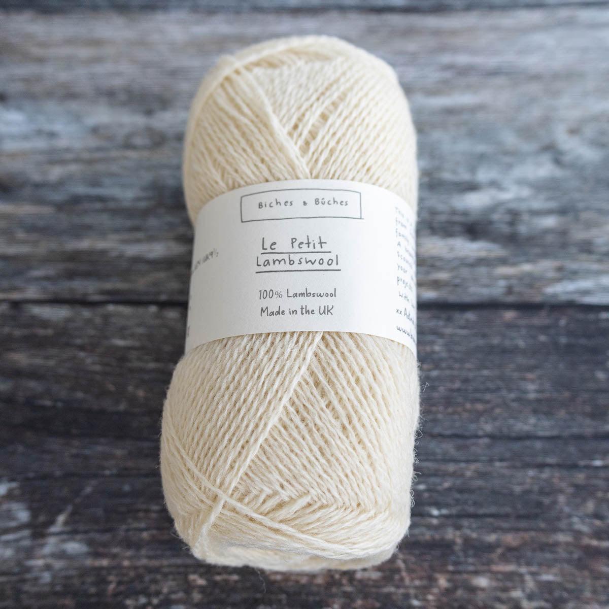 Several skeins of Biches & Büches Le Petit Lambswool yarn in various colors arranged on a wooden surface.